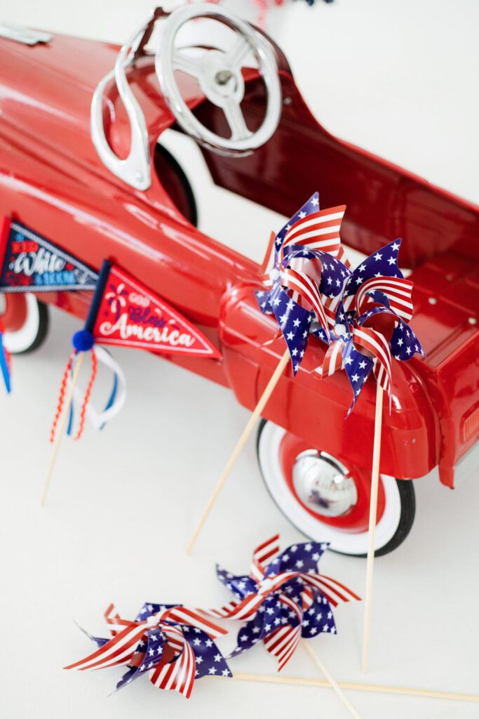 Vintage red toy car with American flags and patriotic photo decorations at Jacksonville studio summer installation.