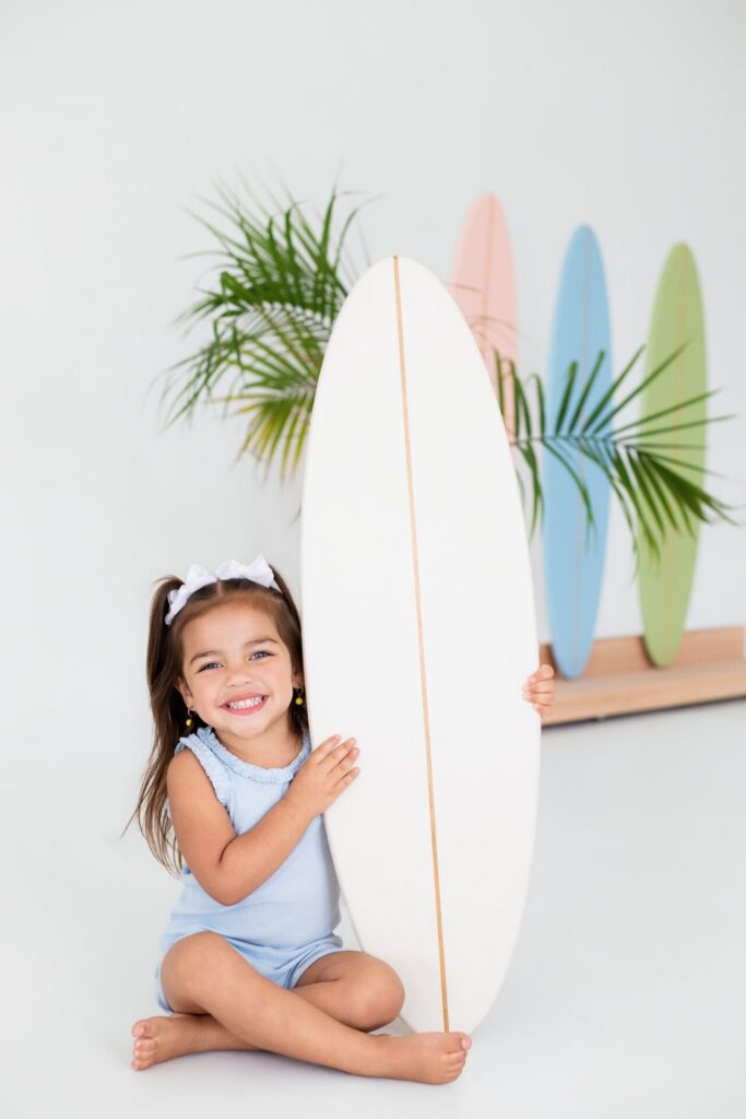 Girl posing with surfboard on beach surfer-inspired photo studio set at Jacksonville natural light studio.
