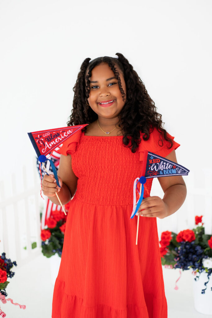 Girl holding patriotic American flags during summer portrait session at Jacksonville photo studio.