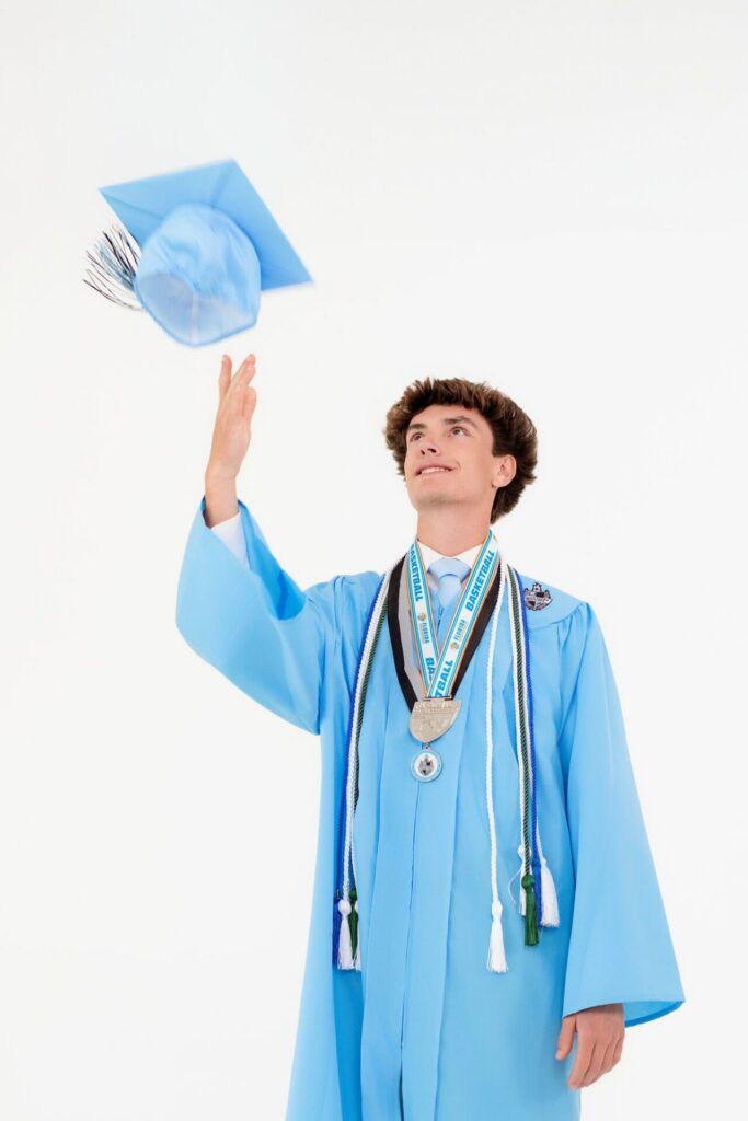 High school graduate tossing cap in the air during fun studio graduation photo session in Jacksonville, FL.