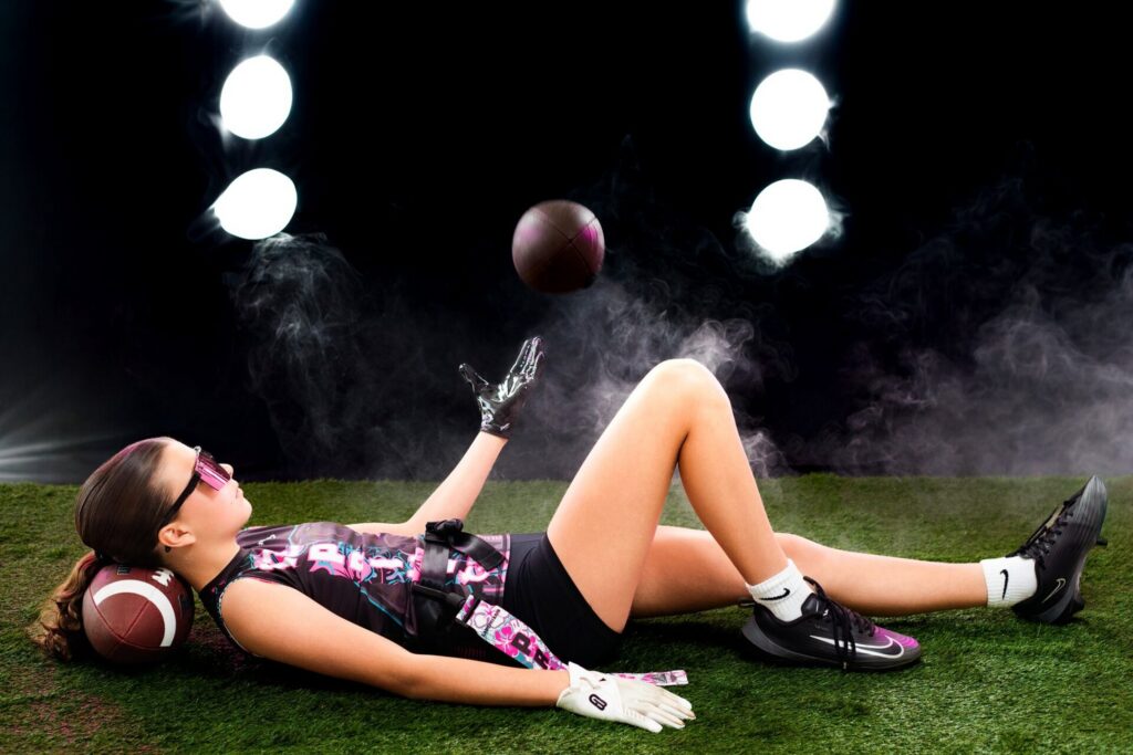 Jacksonville sports photo studio with artificial turf, stadium lights, and fog effects featuring athlete tossing football during sports media day photography session.