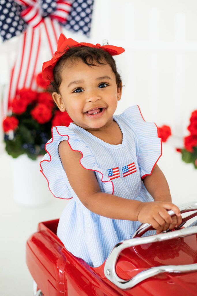 4th of July toddler portrait session featuring child sitting in vintage red car at Jacksonville studio.