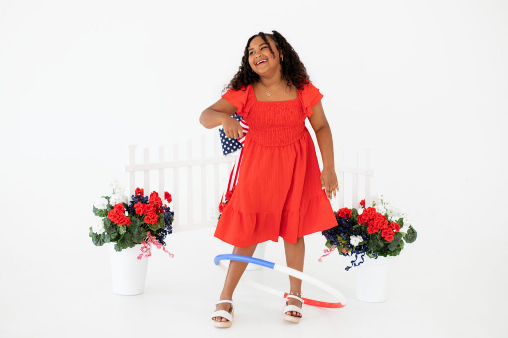 Girl playing with red, white, and blue hula hoop during patriotic portrait session at Jacksonville photo studio.