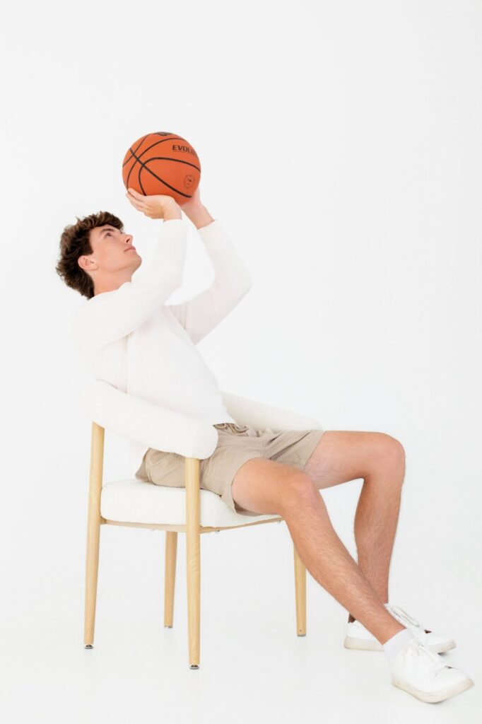 Senior graduate headshot in clean white studio featuring student sitting with basketball to showcase athlete personality during Jacksonville, FL graduation session.