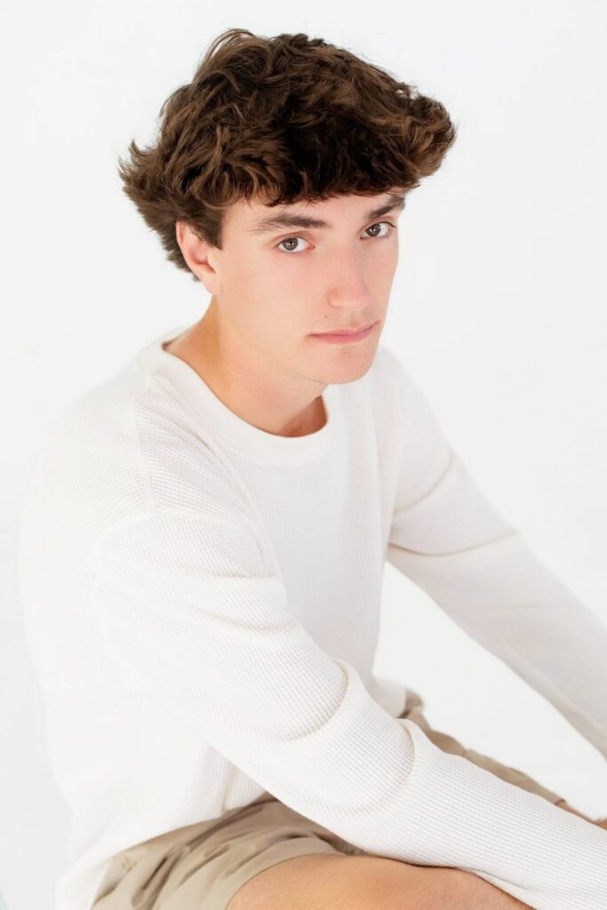 Clean white studio senior graduate headshot of student sitting and looking at camera during graduation portrait session in Jacksonville, FL.