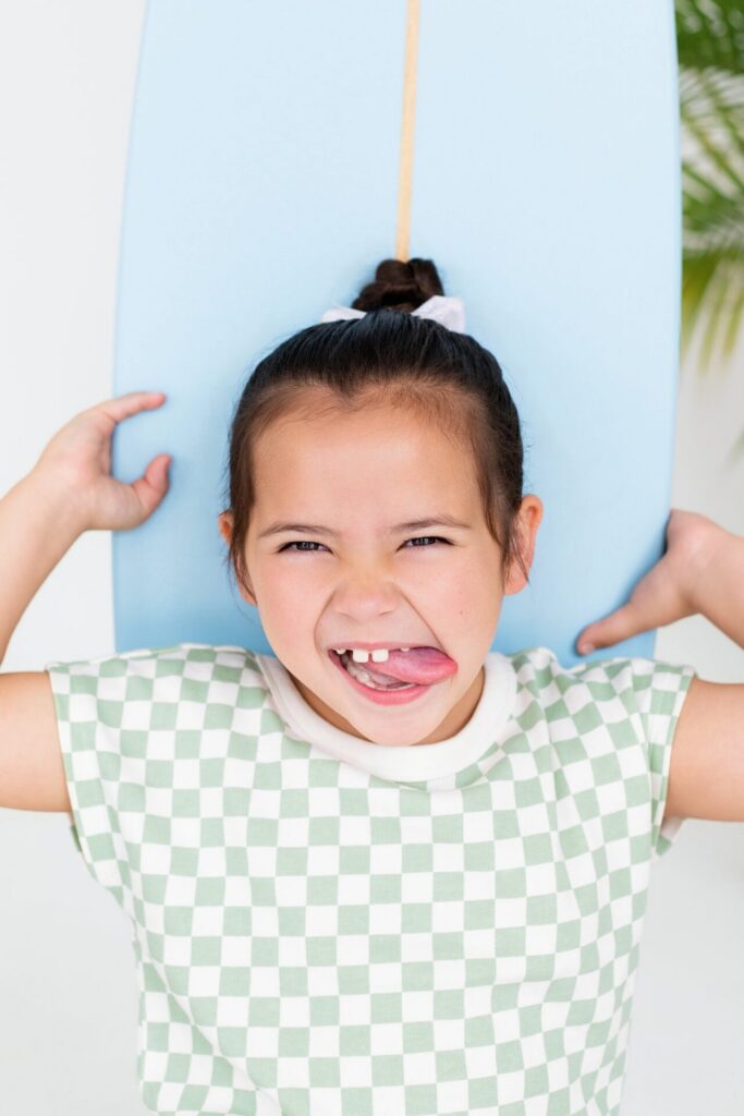 Girl making silly face with surfboard during beach-inspired summer photo session at Jacksonville photo studio.