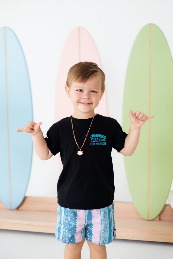 Young boy showing shaka sign during beach-inspired summer photo session with surfer vibe at Jacksonville natural light studio.