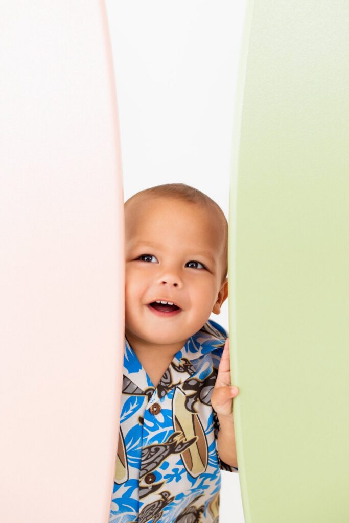 Toddler peeking between surfboards during beach-inspired summer photo session at Jacksonville coastal photo studio.