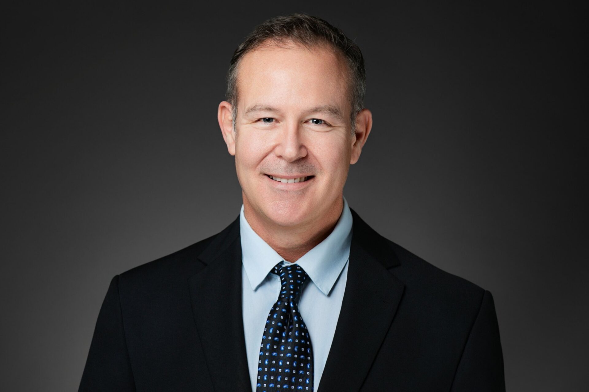 Professional headshot of a man in a suit against a black backdrop