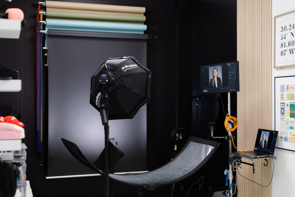 Professional headshots setup at Jax Mini Sessions Studio in Jacksonville, FL featuring black backdrop, Profoto flash, eyelighter, backlight, and tethered camera and monitor setup.