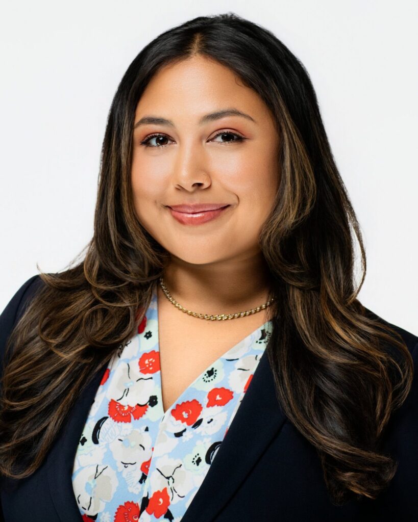 Woman wearing a patterned floral blouse and smiling softly for a professional headshot on a light backdrop.