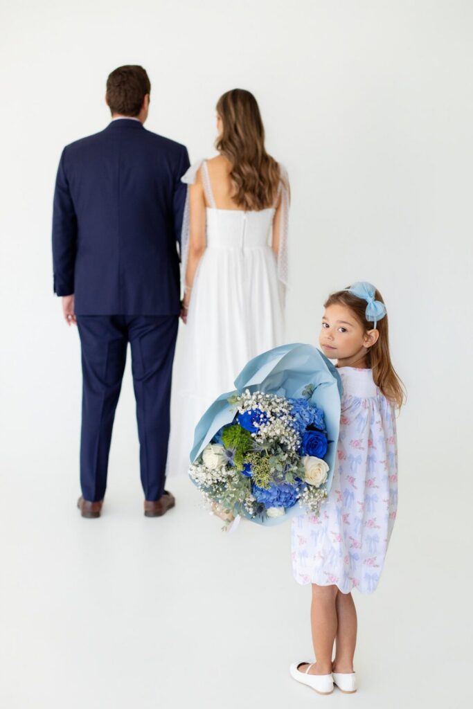 Young daughter looking back at camera while holding a blue gender reveal flower bouquet to hand to mom and dad.