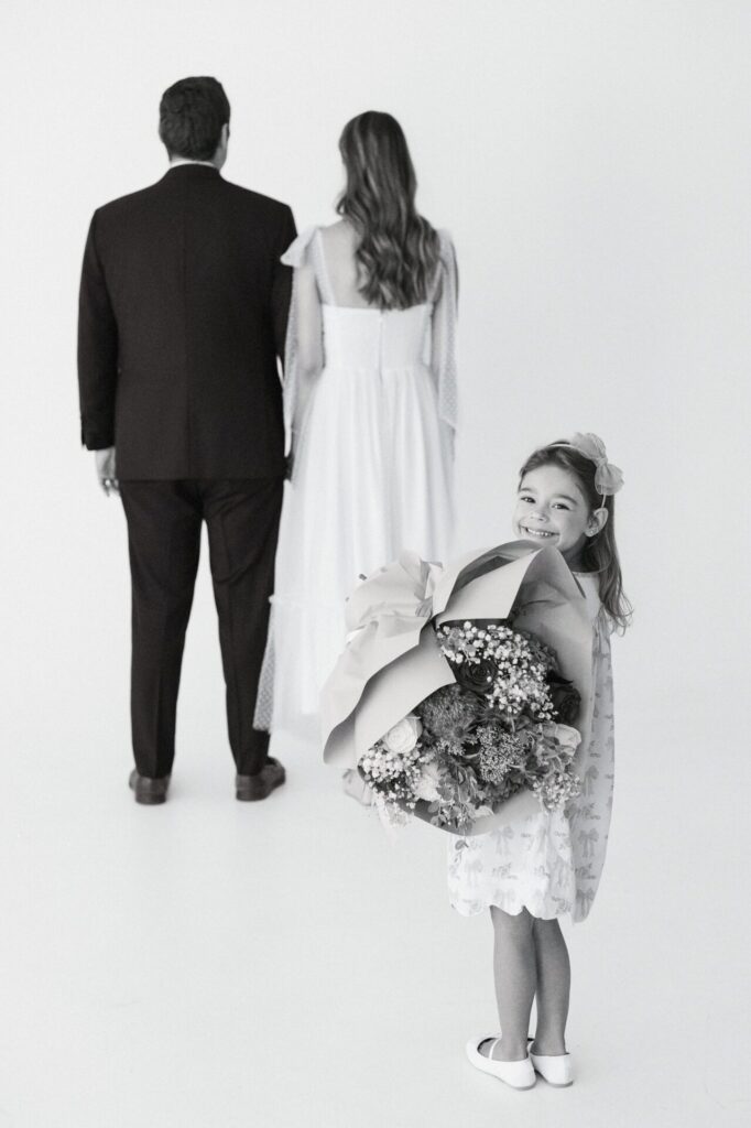 Black and white photo of a gender reveal moment, in which daughter is holding either blue or pink flowers to present to mom and dad. 