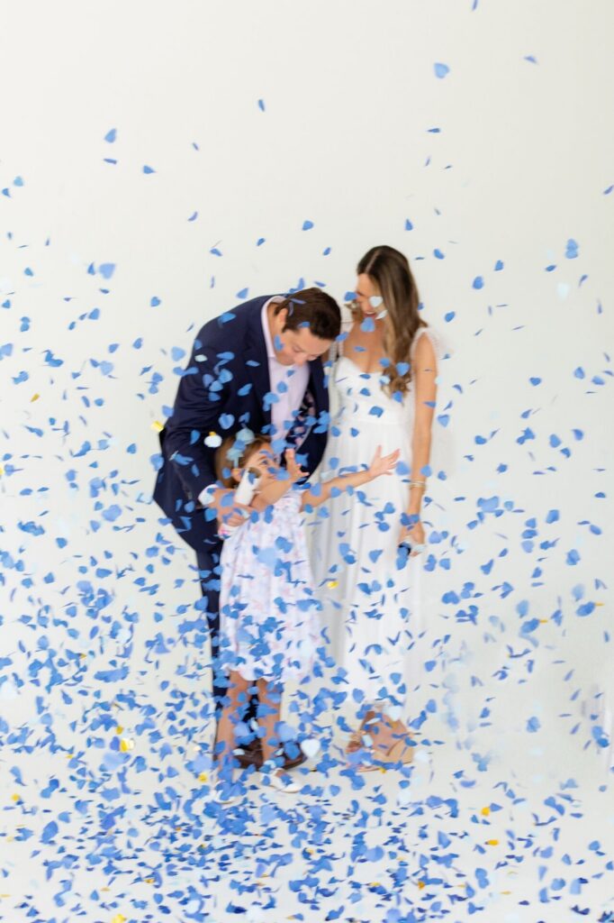 Blue confetti fills the room during an exciting gender reveal at a Jacksonville indoor photo studio.