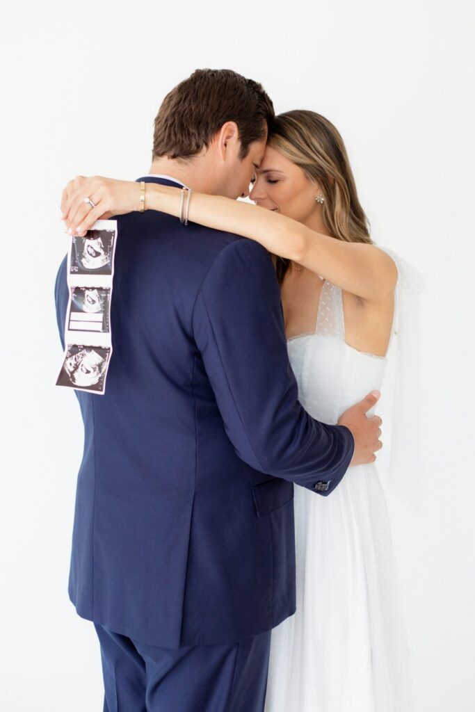 Expecting parents embrace while showing off pregnancy ultrasound in a Jacksonville, FL photo studio.