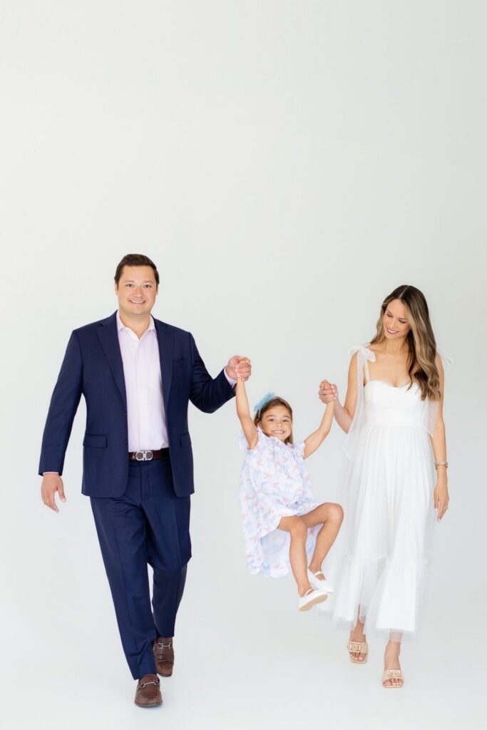 Parents swing their daughter during a joyful family portrait before their gender reveal at a Jacksonville photo studio.