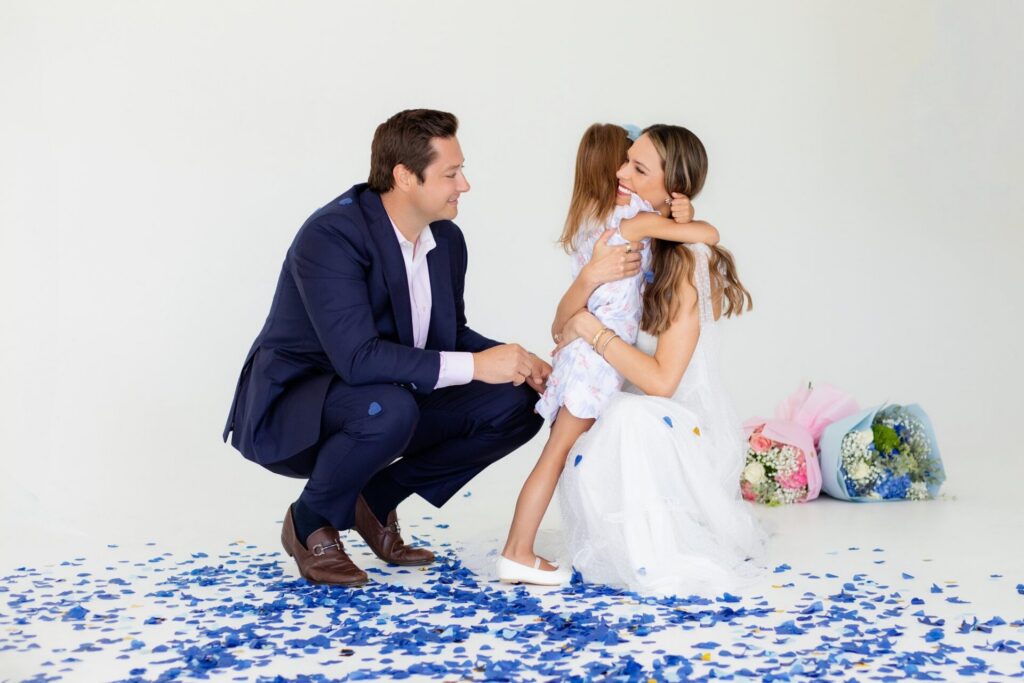 Family celebrating a baby boy during a Jacksonville gender reveal photo session as a daughter hugs her mom after the blue confetti reveal.
