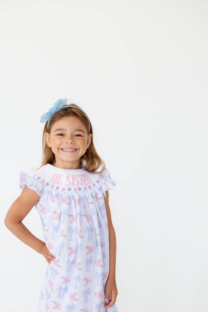 Young girl smiles and poses for a studio portrait wearing a "Big Sister" dress during pregnancy gender reveal photoshoot. 