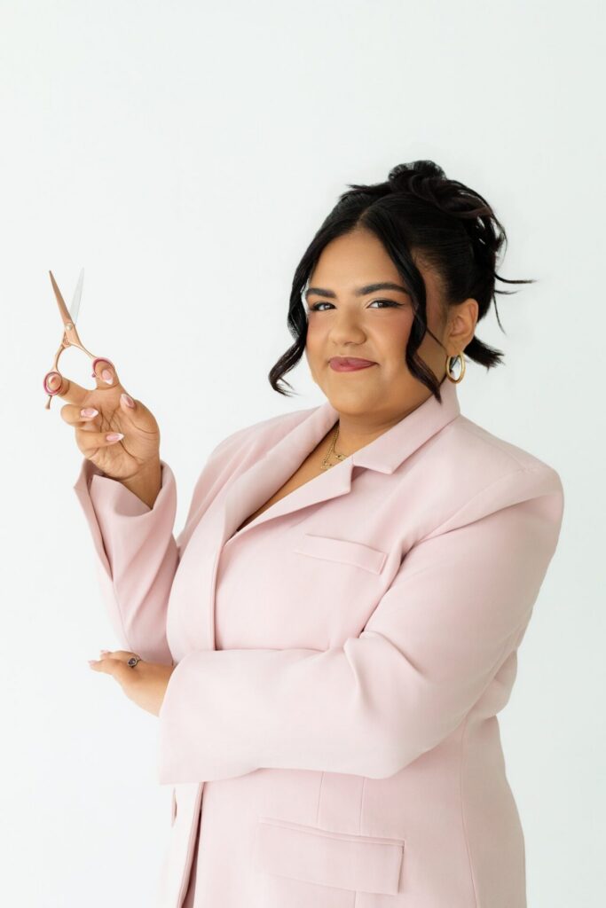 Young hair stylist holding a pair of scissors and posing for a personality headshot photo during a branding session at Jacksonville indoor photo studio.