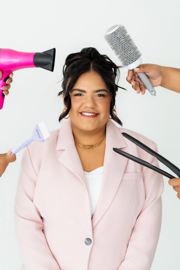 Hair stylist smiling for a professional photo with different hair tools being held up around her face for a branding session.