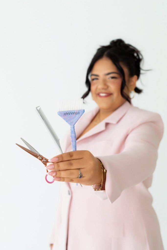 Hair stylist holding tools like scissors and comb in focus in front of her face in all natural indoor studio branding photo session.