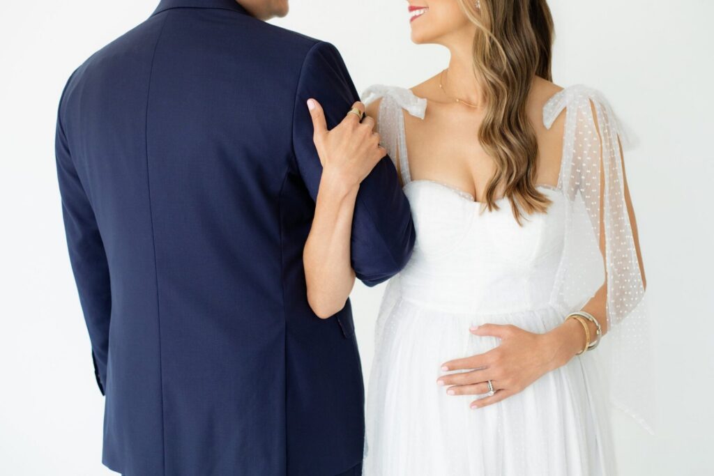 Expectant parents embrace during a pregnancy announcement photo session at a Jacksonville photo studio, with mom holding her baby bump.